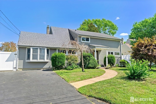 traditional home with a front yard, roof with shingles, fence, and a chimney