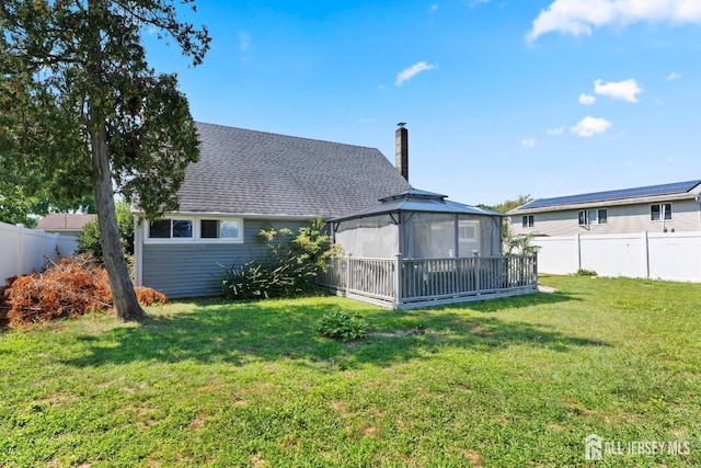 back of house featuring a fenced backyard, a gazebo, a lawn, roof with shingles, and a chimney