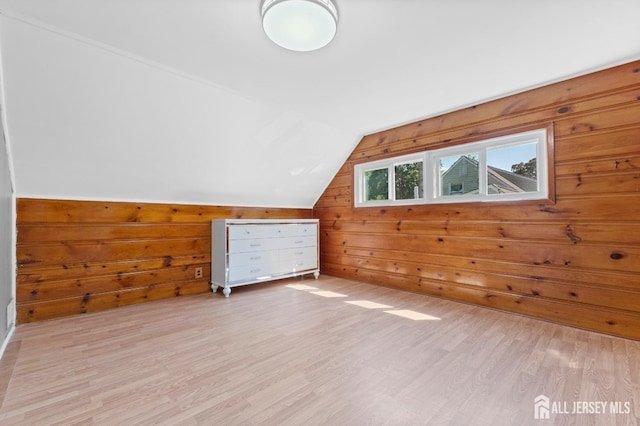 bonus room with light wood-style flooring, wooden walls, and vaulted ceiling