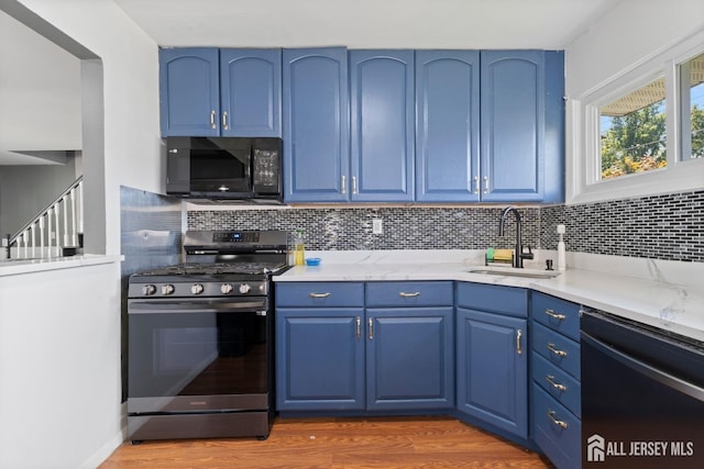 kitchen featuring black microwave, blue cabinets, a sink, dishwasher, and gas range