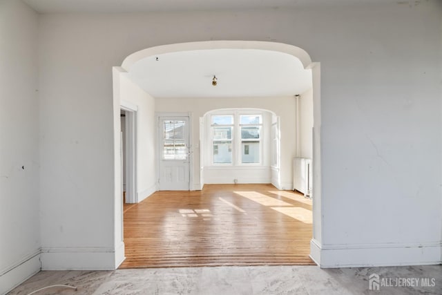 foyer entrance with radiator, arched walkways, and wood finished floors