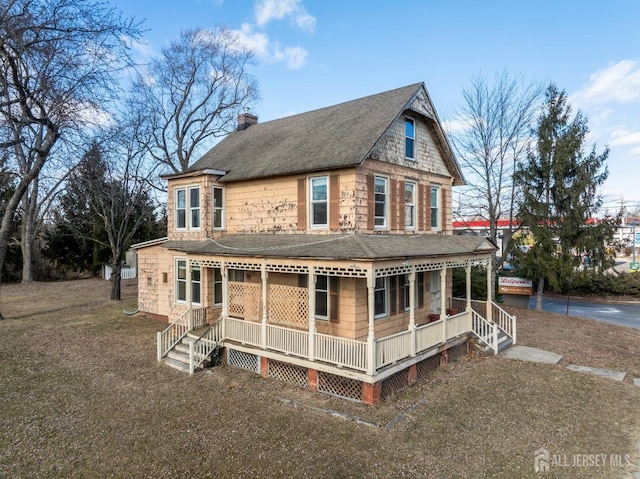 back of house featuring covered porch, a shingled roof, and a chimney