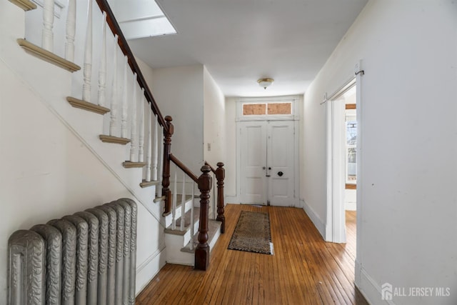 entrance foyer featuring wood-type flooring, stairway, radiator heating unit, and baseboards