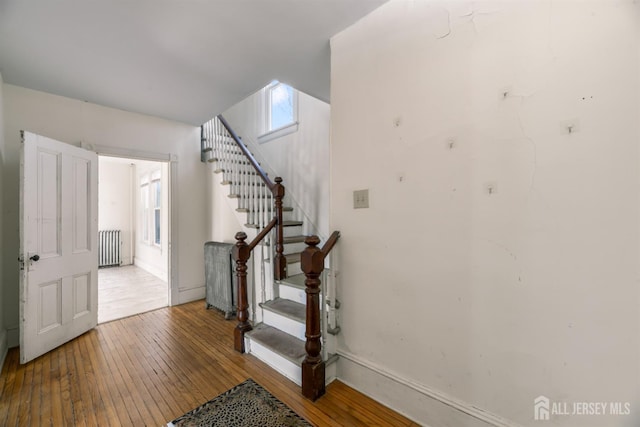 stairs with radiator heating unit, wood-type flooring, and baseboards