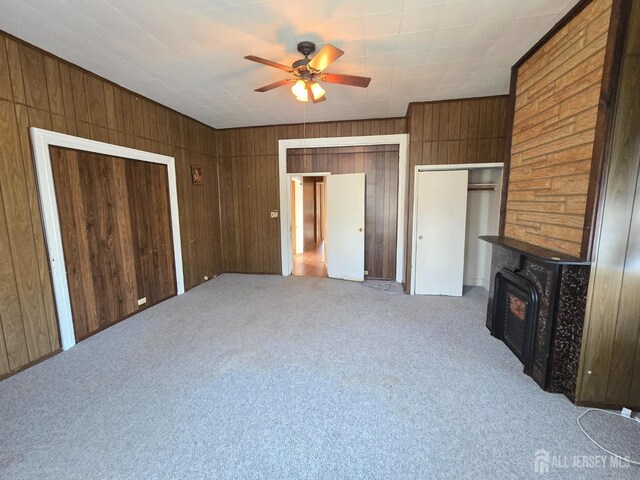 unfurnished bedroom with light colored carpet, a fireplace, wood walls, and two closets