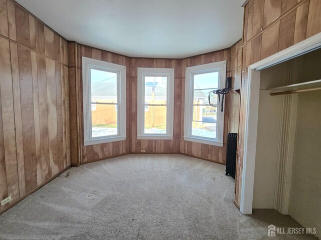 unfurnished room featuring light colored carpet, radiator heating unit, and wooden walls