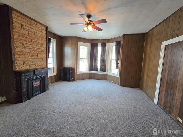 unfurnished living room with wood walls, radiator heating unit, light carpet, and a wood stove