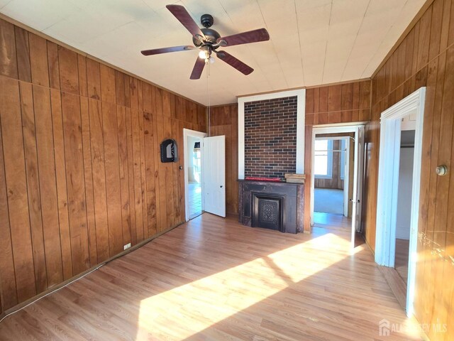 unfurnished living room with ceiling fan, light hardwood / wood-style floors, and wood walls