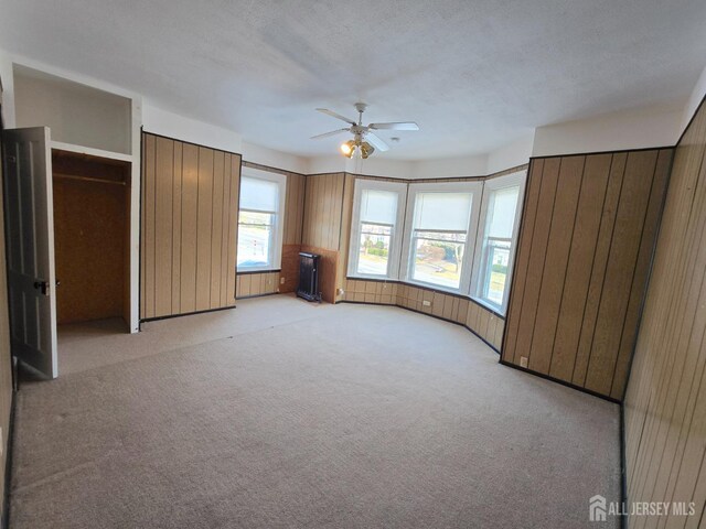 unfurnished bedroom featuring ceiling fan, wooden walls, light carpet, and a textured ceiling