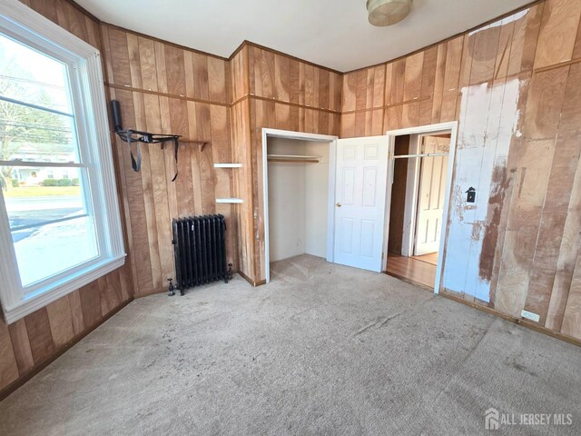 unfurnished bedroom featuring light carpet, radiator heating unit, and wood walls