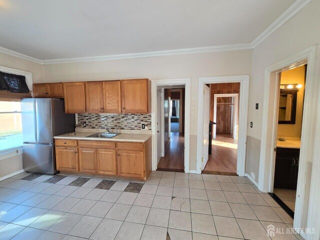 kitchen featuring crown molding, sink, light tile patterned floors, and stainless steel refrigerator