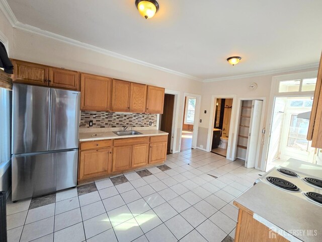 kitchen with stainless steel refrigerator, sink, decorative backsplash, light tile patterned floors, and crown molding