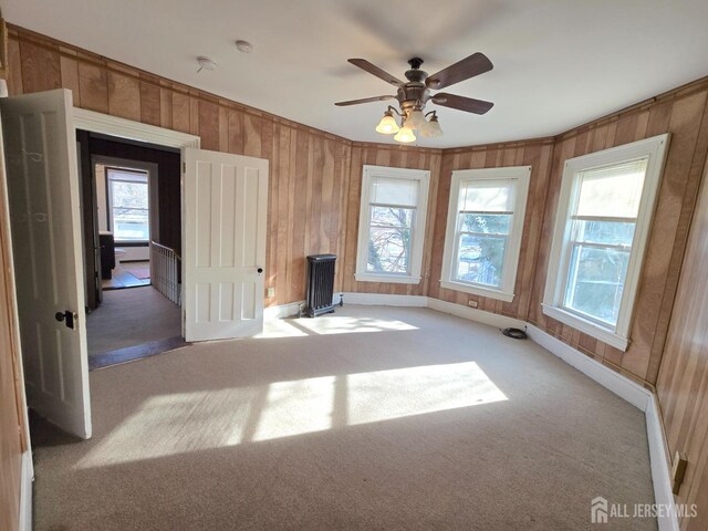 unfurnished living room with a wealth of natural light, light colored carpet, ceiling fan, and wooden walls