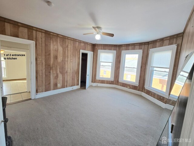 carpeted empty room with ceiling fan and wood walls