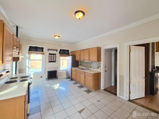 kitchen featuring crown molding, light tile patterned floors, radiator heating unit, stainless steel fridge, and range with electric cooktop