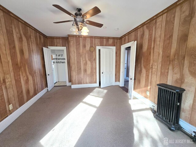 carpeted empty room with ornamental molding, ceiling fan, and wood walls