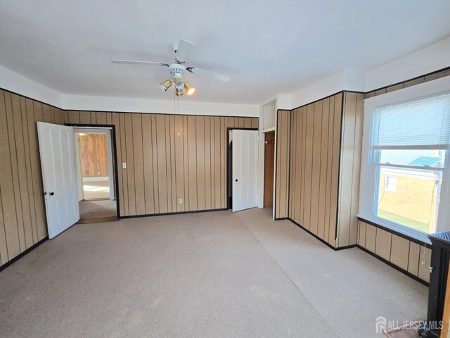 unfurnished bedroom with light carpet, wooden walls, and ceiling fan