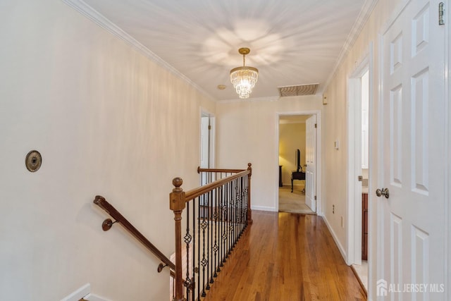 corridor with crown molding, wood-type flooring, and a notable chandelier