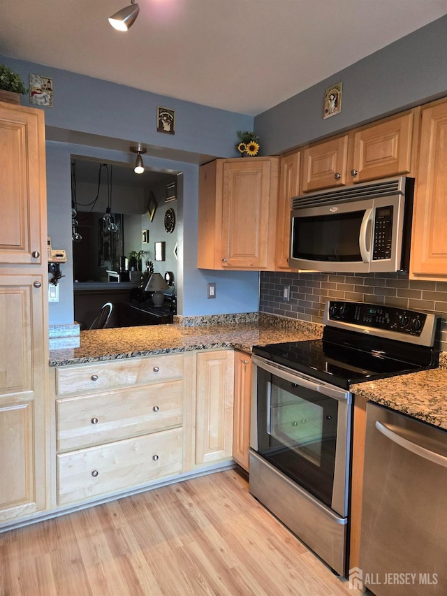 kitchen with light stone countertops, appliances with stainless steel finishes, decorative backsplash, light brown cabinetry, and light hardwood / wood-style floors