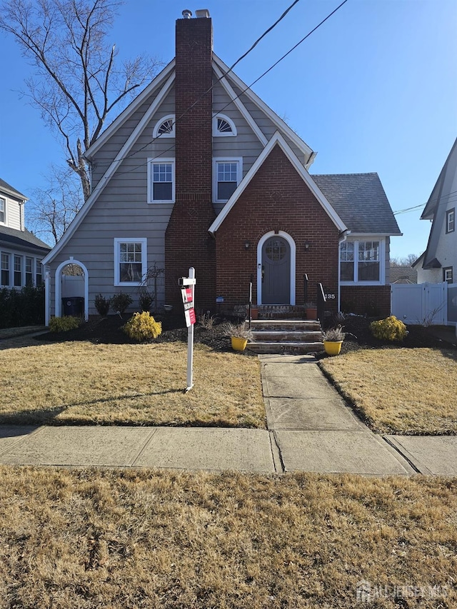 view of front facade with a front lawn, fence, brick siding, and a chimney