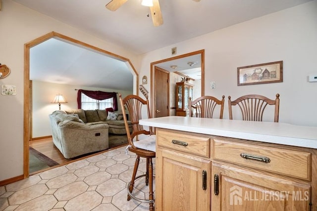 kitchen featuring ceiling fan, a breakfast bar, light countertops, baseboards, and open floor plan