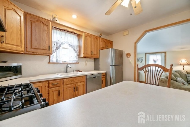 kitchen with appliances with stainless steel finishes, a sink, a ceiling fan, light countertops, and arched walkways