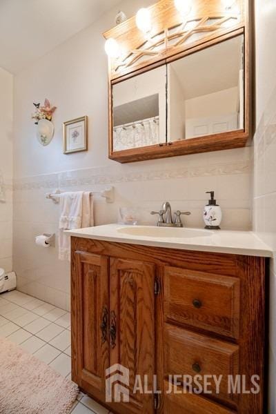 bathroom with tile walls, vanity, tile patterned flooring, and wainscoting