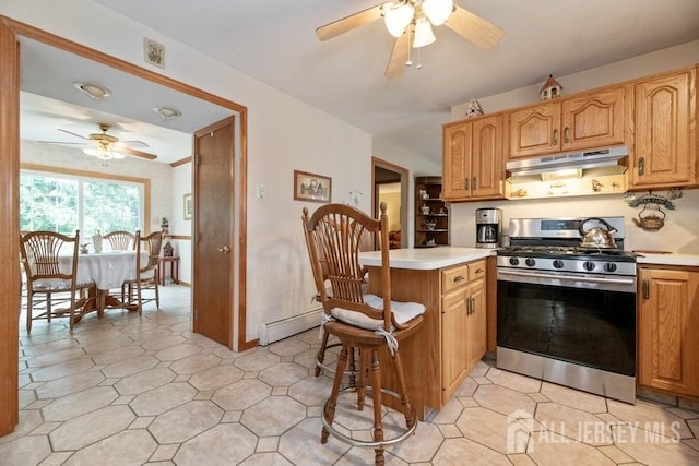 kitchen featuring gas stove, under cabinet range hood, a ceiling fan, light countertops, and a breakfast bar