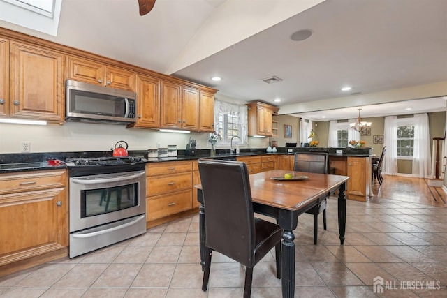 kitchen with a sink, dark countertops, stainless steel appliances, a peninsula, and brown cabinetry