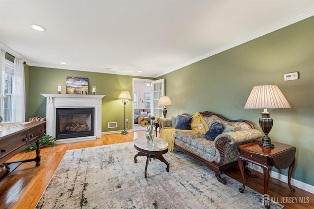 living area with visible vents, ornamental molding, wood finished floors, a glass covered fireplace, and baseboards