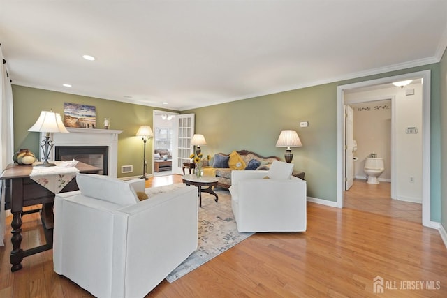 living area featuring visible vents, baseboards, ornamental molding, light wood-style floors, and a glass covered fireplace