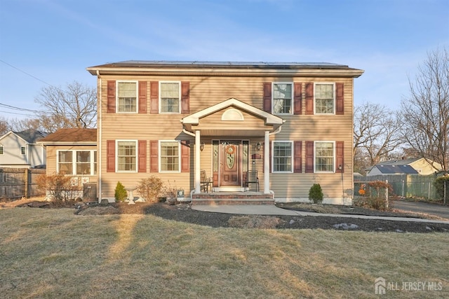 view of front of house with roof mounted solar panels, a front yard, and fence