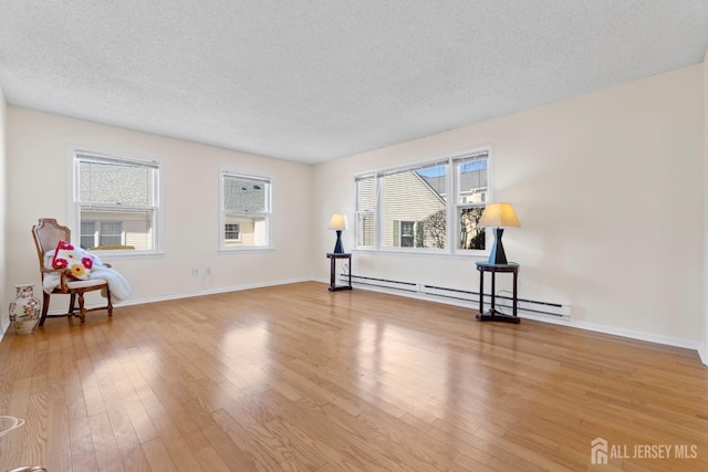 living area with light wood-style floors, a baseboard radiator, baseboards, and a textured ceiling