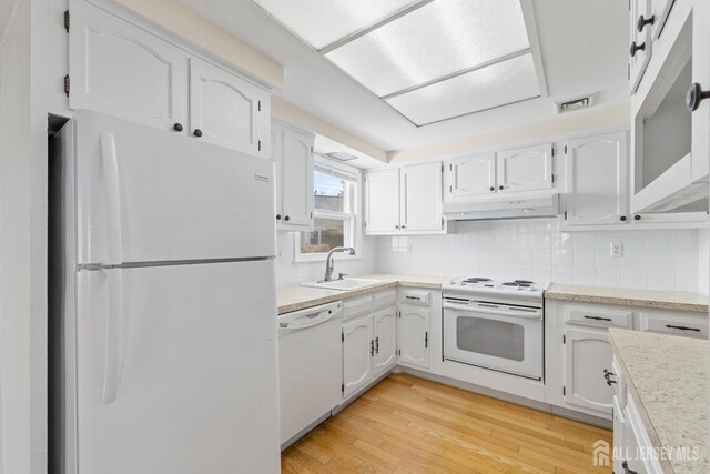 kitchen featuring white appliances, white cabinets, light wood-style flooring, under cabinet range hood, and a sink