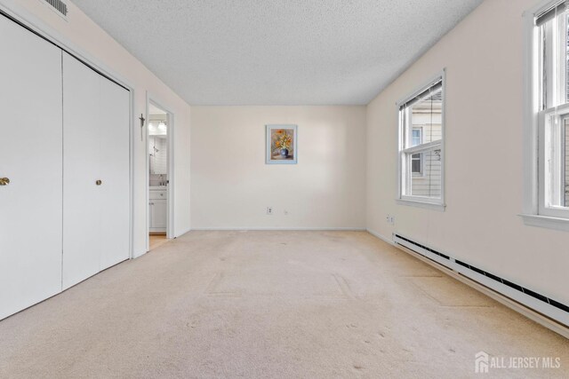 unfurnished bedroom with multiple windows, a baseboard heating unit, and a textured ceiling