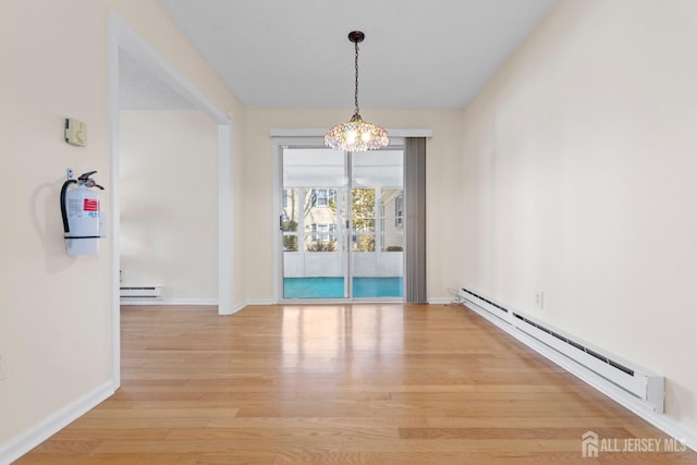 unfurnished dining area featuring baseboards, an inviting chandelier, baseboard heating, light wood-style floors, and a baseboard heating unit