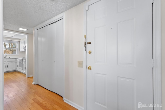 corridor featuring light wood-style flooring, a sink, and a textured ceiling