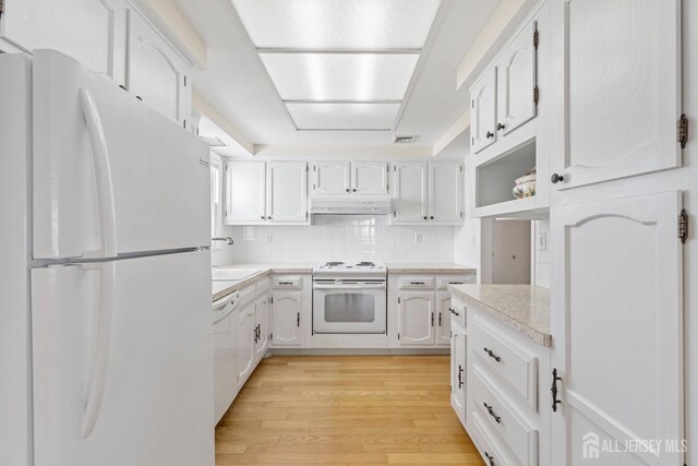 kitchen with light wood-style flooring, under cabinet range hood, white appliances, a sink, and light countertops