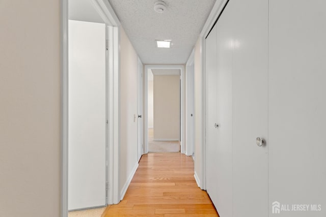 corridor featuring light wood finished floors, baseboards, and a textured ceiling