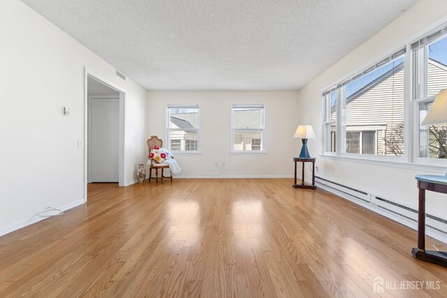 unfurnished room featuring visible vents, baseboard heating, a textured ceiling, light wood-type flooring, and baseboards