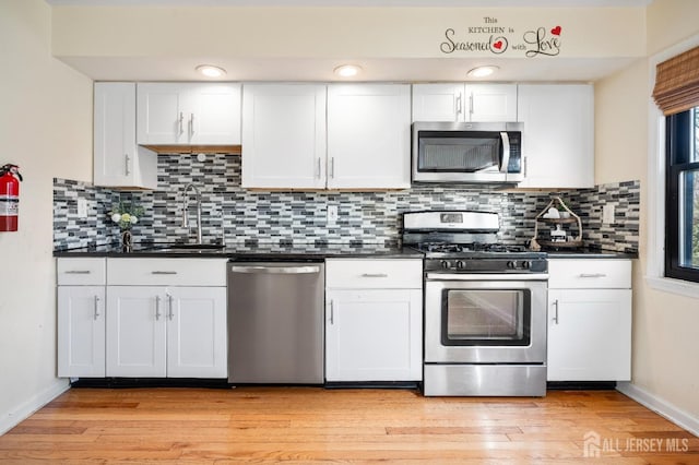 kitchen with appliances with stainless steel finishes, dark countertops, a sink, baseboards, and white cabinets