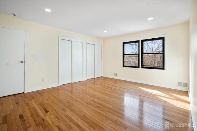 unfurnished bedroom featuring two closets, light wood finished floors, baseboards, and recessed lighting