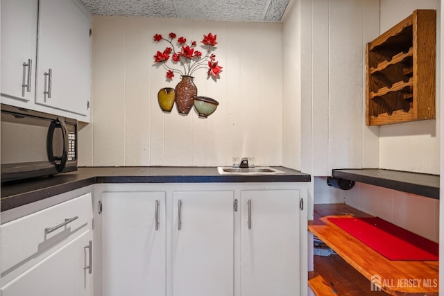 kitchen featuring a sink, black microwave, dark countertops, white cabinets, and a decorative wall