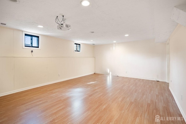 below grade area with light wood-style floors, plenty of natural light, baseboards, a textured ceiling, and recessed lighting