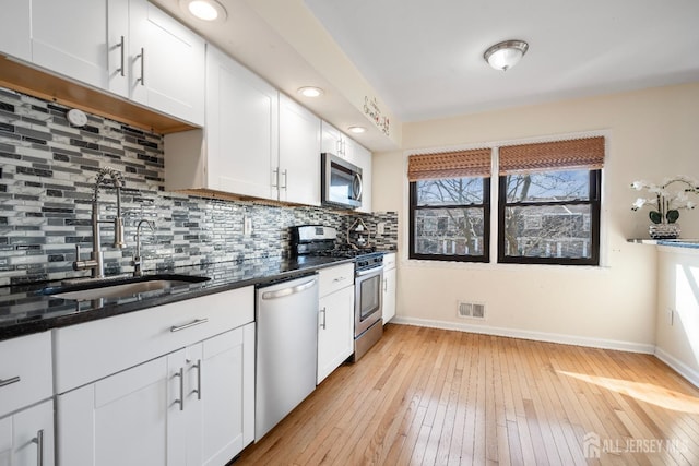kitchen featuring appliances with stainless steel finishes, a sink, dark countertops, light wood-style flooring, and baseboards