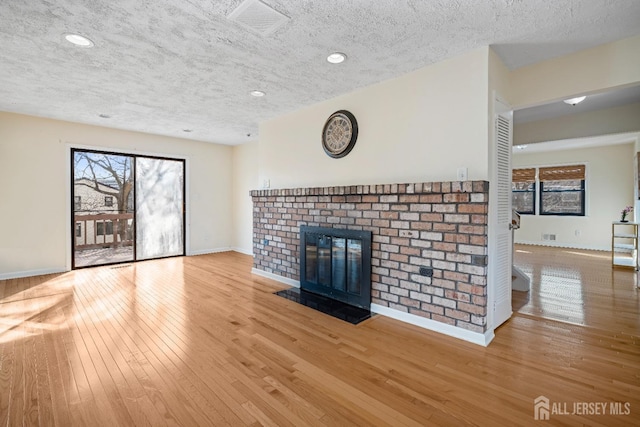 unfurnished living room with baseboards, hardwood / wood-style floors, a textured ceiling, a brick fireplace, and recessed lighting
