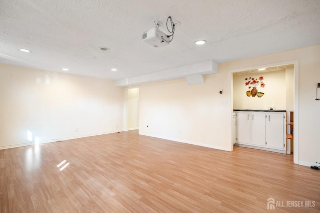 unfurnished room with a textured ceiling, light wood-style flooring, recessed lighting, and baseboards