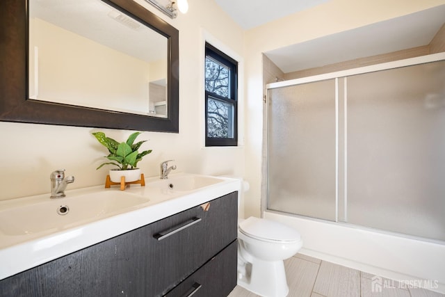 bathroom featuring double vanity, toilet, and shower / bath combination with glass door
