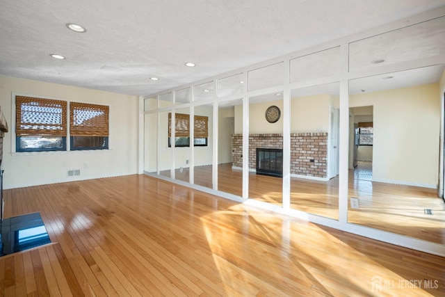 unfurnished living room with wood-type flooring, a fireplace, recessed lighting, and a textured ceiling