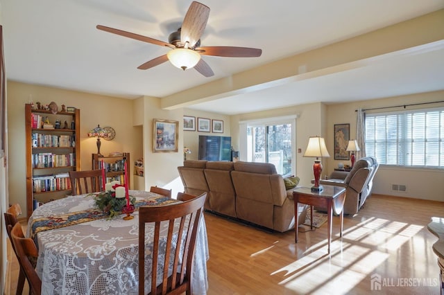 dining space with ceiling fan, a wealth of natural light, beamed ceiling, and light hardwood / wood-style flooring